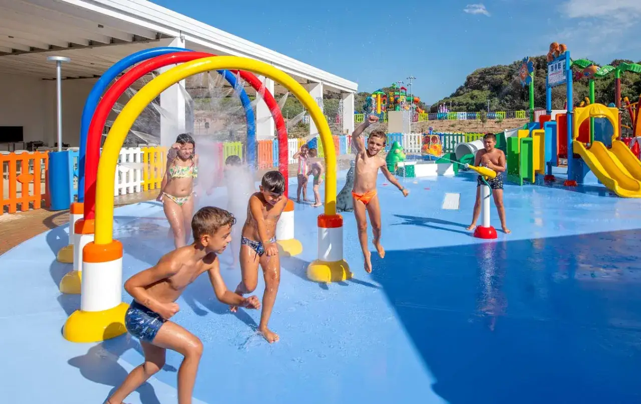 Bambini felici giocano nell'acqua in un parco acquatico in Sardegna, tra spruzzi e scivoli colorati.