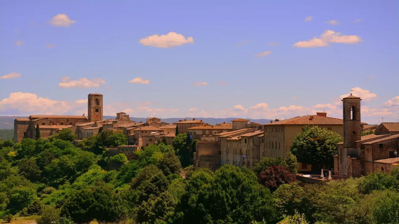 Panoramica di Colle Val d'Elsa, con torri medievali e tetti in cotto che emergono da una rigogliosa vegetazione.