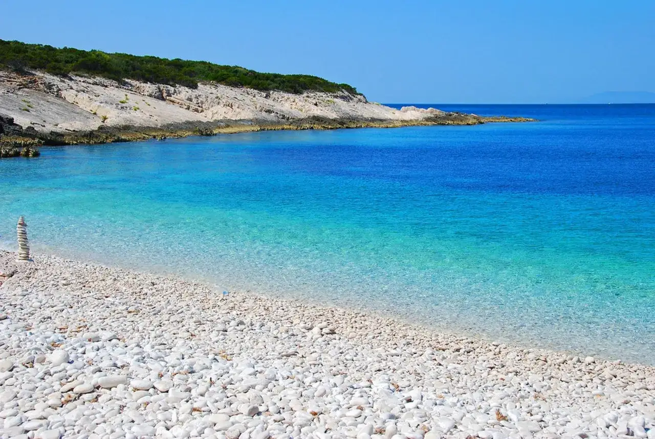 Spiaggia di ciottoli bianchi e mare cristallino, un angolo di Croazia mare pi&ugrave; bello con rocce e vegetazione mediterranea.