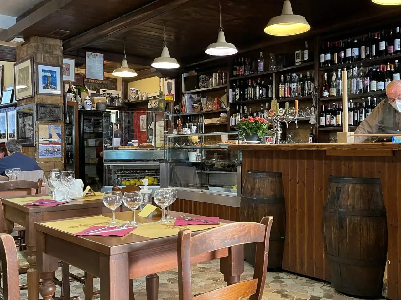 Tavoli apparecchiati in un locale accogliente, ideale per chi cerca dove mangiare a Padova spendendo poco. Bottiglie e botti creano un'atmosfera rustica.