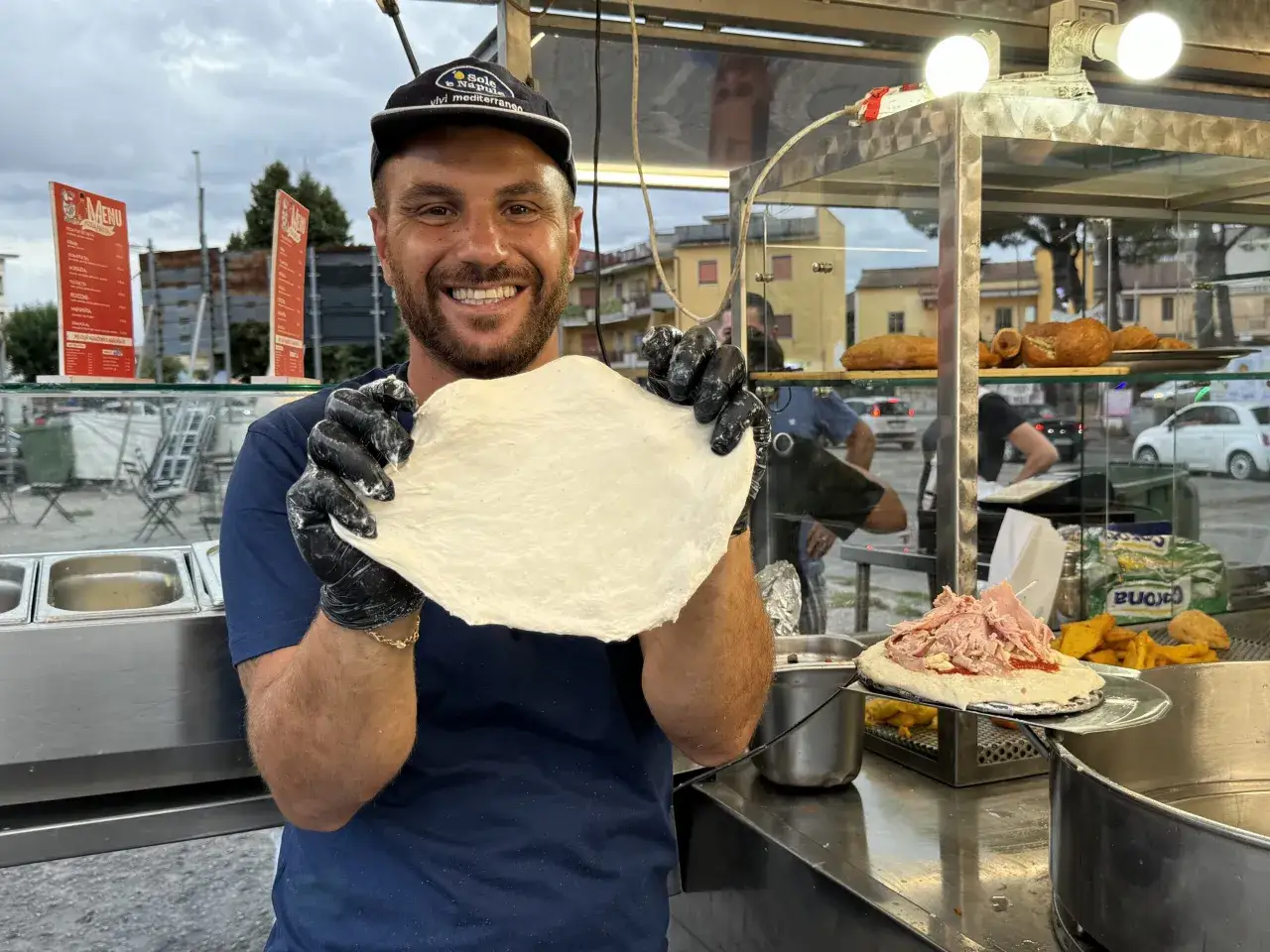 Un pizzaiolo sorridente mostra un impasto per pizza, pronto per preparare deliziose specialità. Ecco cosa mangiare a Napoli!