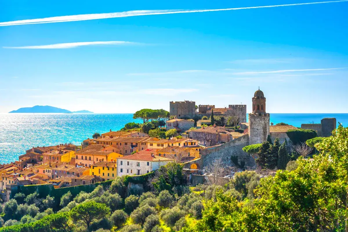 Panoramica di Castiglione della Pescaia, con case colorate, un castello medievale e il mare blu intenso.