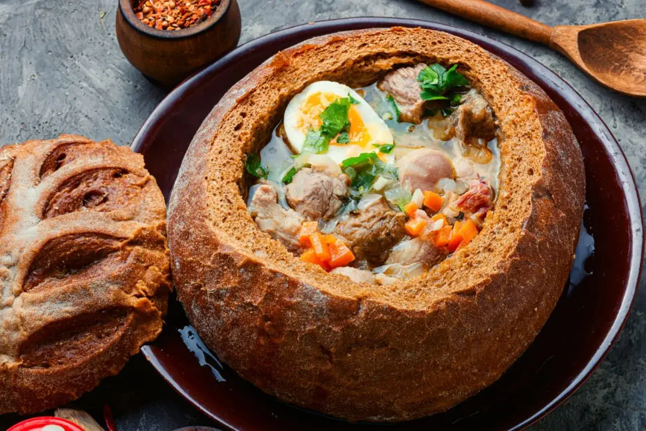 Zuppa servita in una pagnotta, un'idea su cosa mangiare a Varsavia. Carne, uova e verdure in un pane croccante.