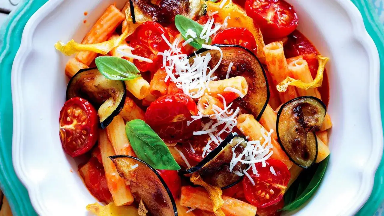 Pasta con melanzane, pomodorini e basilico, un classico dei piatti tipici della Sicilia, guarnita con ricotta salata grattugiata.