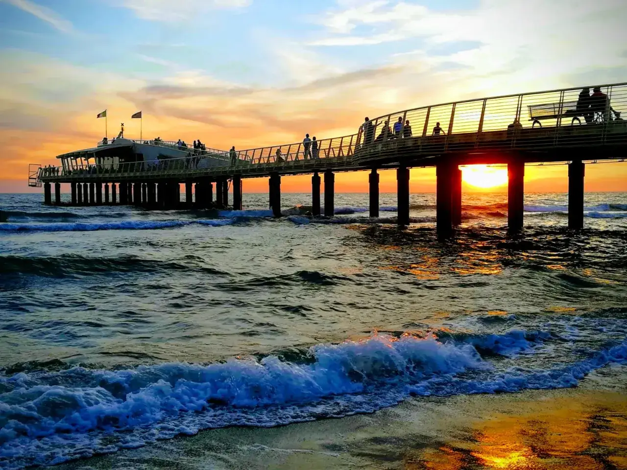 Tramonto sul mare a Camaiore, con gente che passeggia sul pontile.