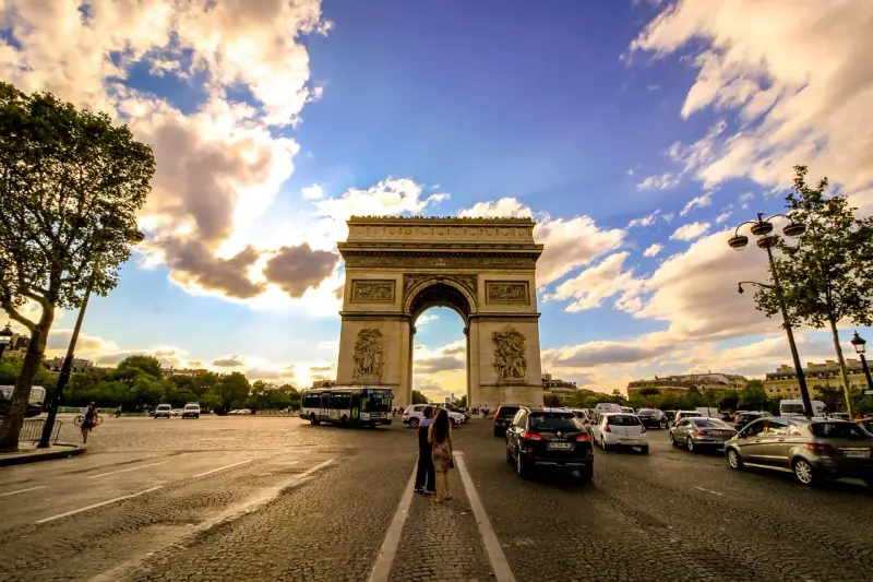 Arco di Trionfo, un'icona di cosa vedere a Parigi, con traffico e nuvole al tramonto.
