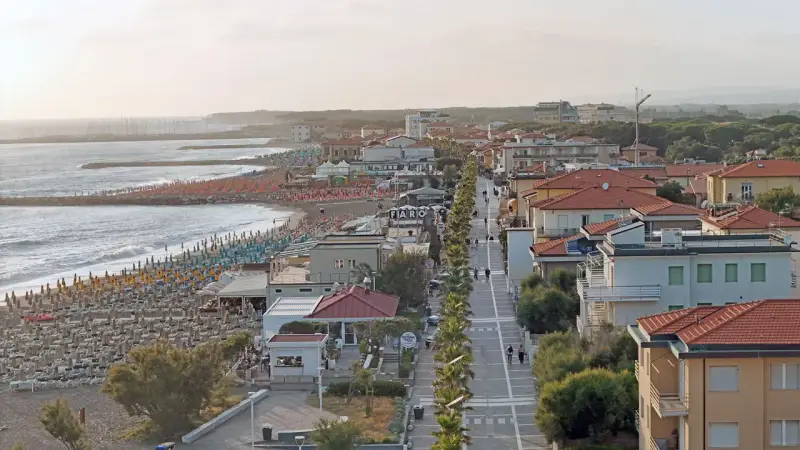 Vista aerea del lungomare di Marina di Cecina con spiaggia attrezzata, mare calmo e case con tetti rossi.