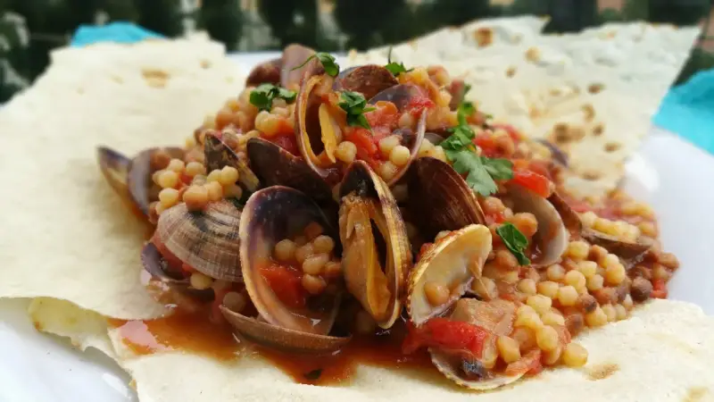 Vongole e fregola, un classico dei piatti tipici sardi, servite su pane carasau croccante.